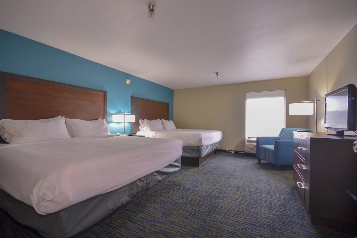 Quarto de hotel com duas camas, uma escrivaninha, uma cadeira e uma televisão.