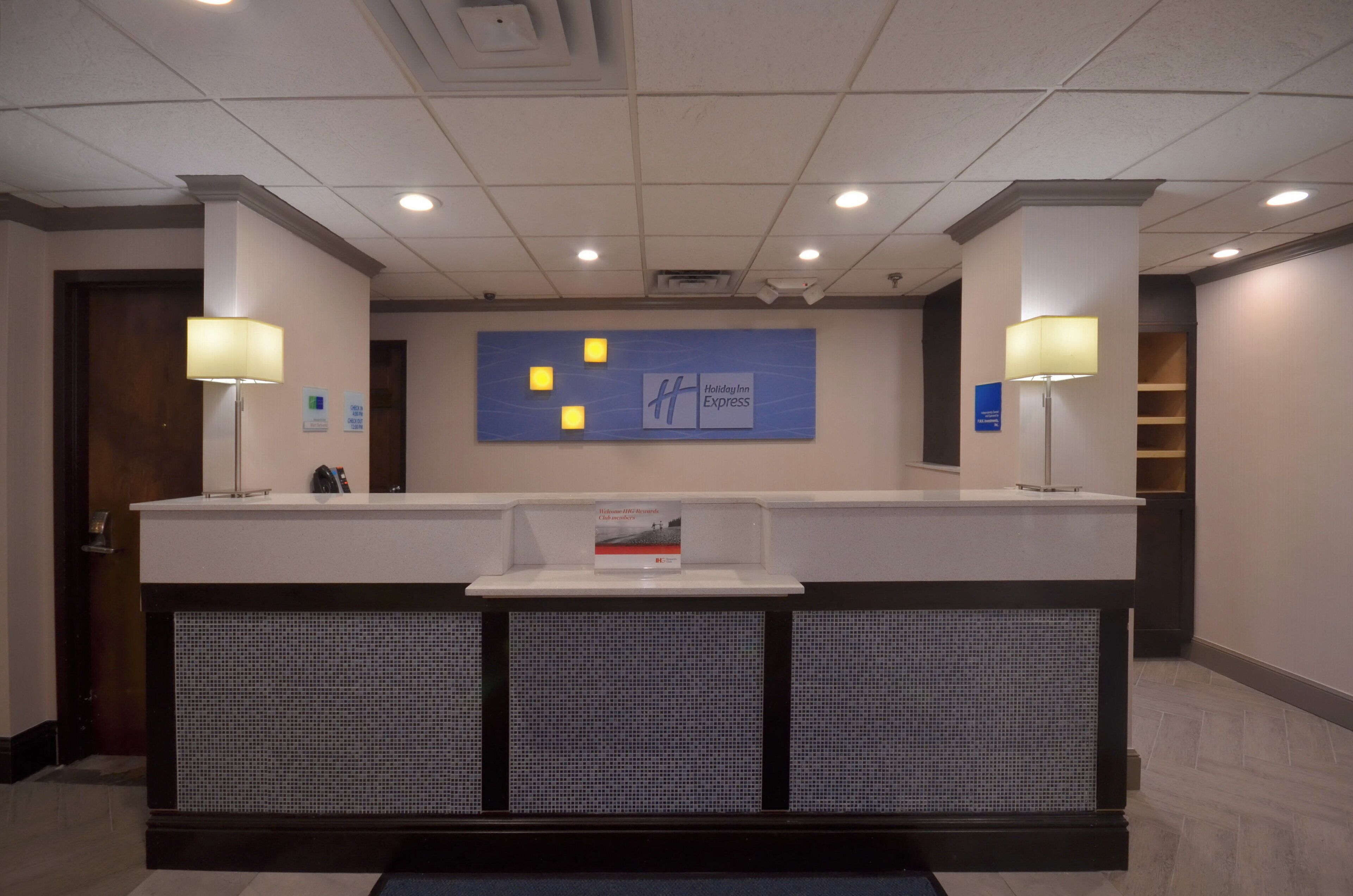 A hotel reception desk with a blue sign, two lamps, and a check-in/out sign.