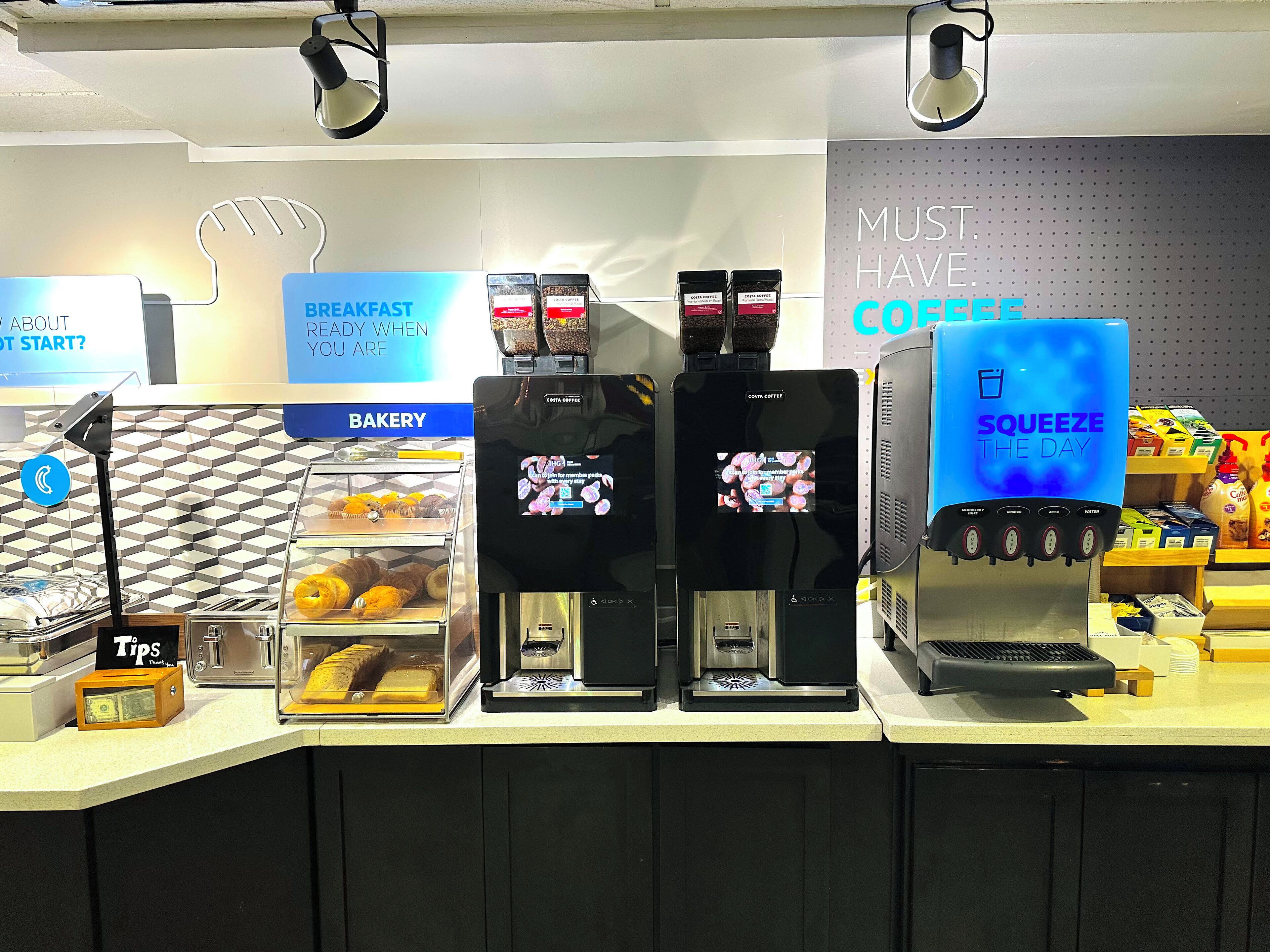 A coffee shop counter with multiple coffee machines, a bakery display, and a sign that reads "MUST HAVE COFFEE".
