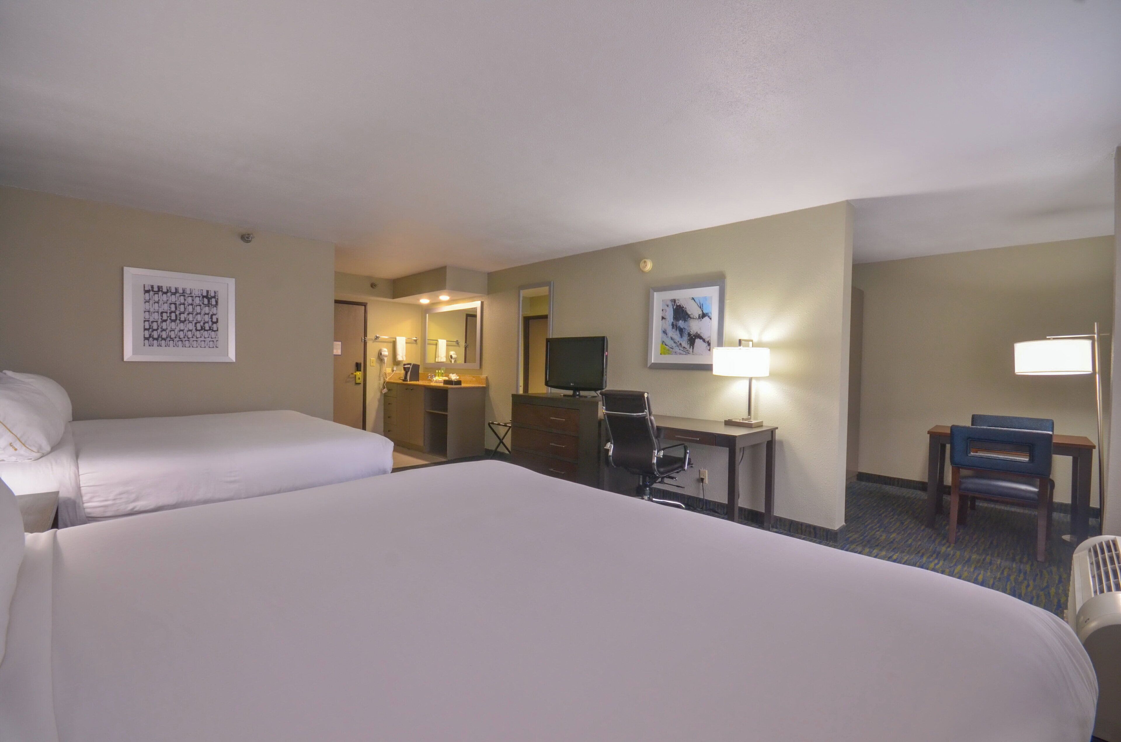 A hotel room with two beds, a desk with a chair, a television, and a bathroom visible through an open door.
