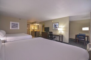 A hotel room with two beds, a desk with a chair, a television, and a bathroom visible through an open door.