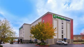 Um hotel Holiday Inn Express com estacionamento e uma árvore na frente.