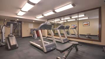 Un gimnasio con cintas de correr, escaladora y banco.