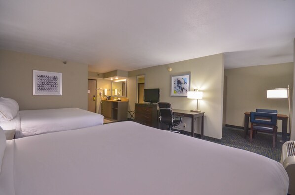 Quarto de hotel com duas camas, uma escrivaninha, uma cadeira, televisão e obras de arte nas paredes.