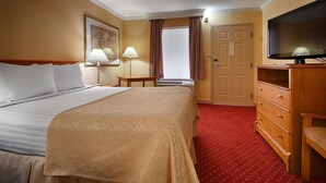 A hotel room with a large bed, a wooden dresser, a television, and a window with curtains.