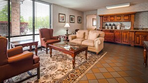 A living room with a sofa, armchairs, a coffee table, and a rug. There is a kitchen area with wooden cabinets and a countertop.