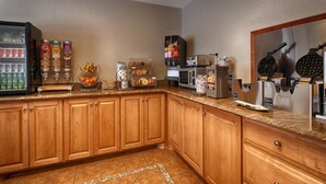 A kitchen with wooden cabinets, a refrigerator, a microwave, a waffle maker, and a coffee machine.
