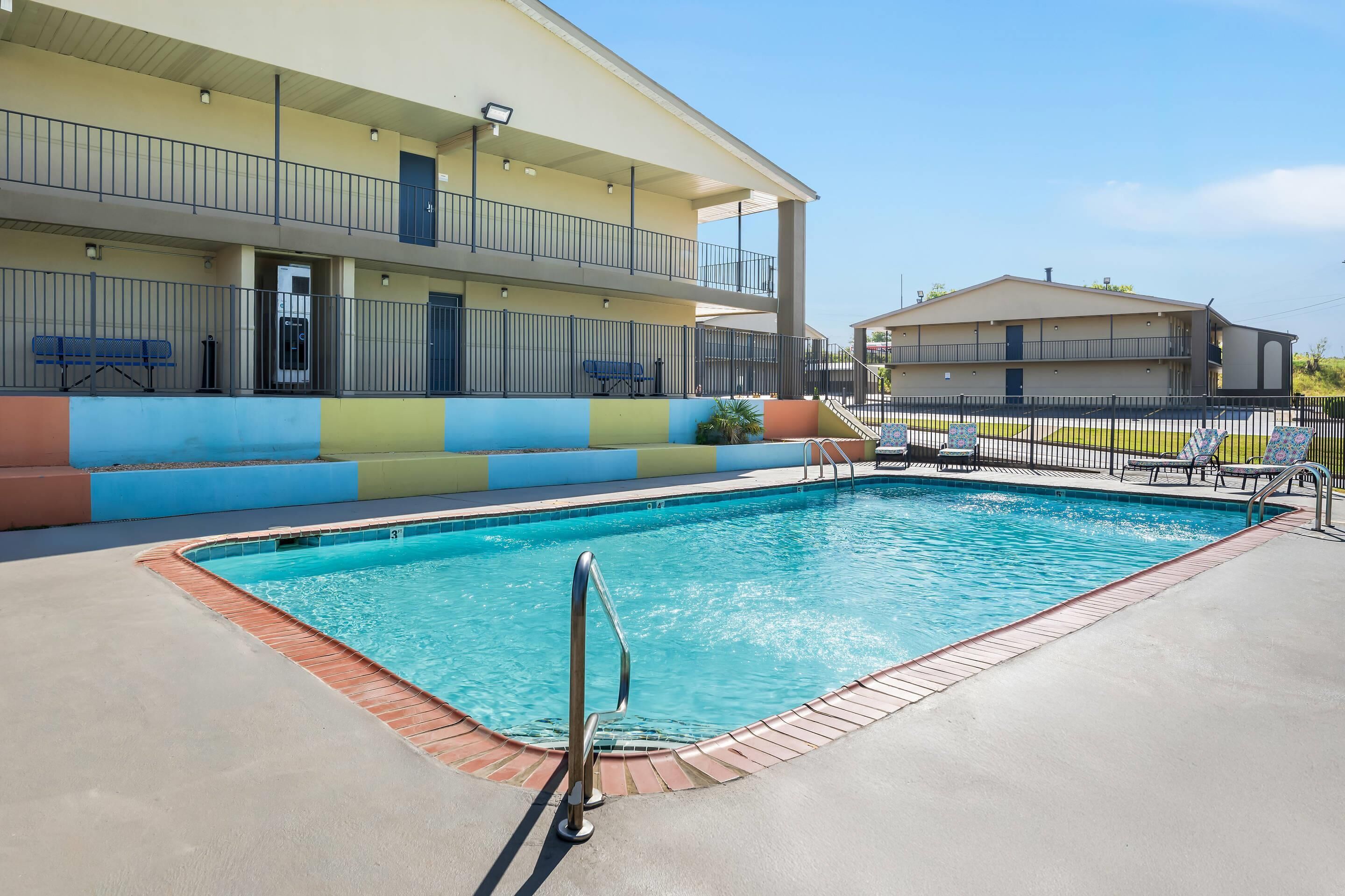 A swimming pool with a metal ladder, a bench, and a building with a balcony in the background.