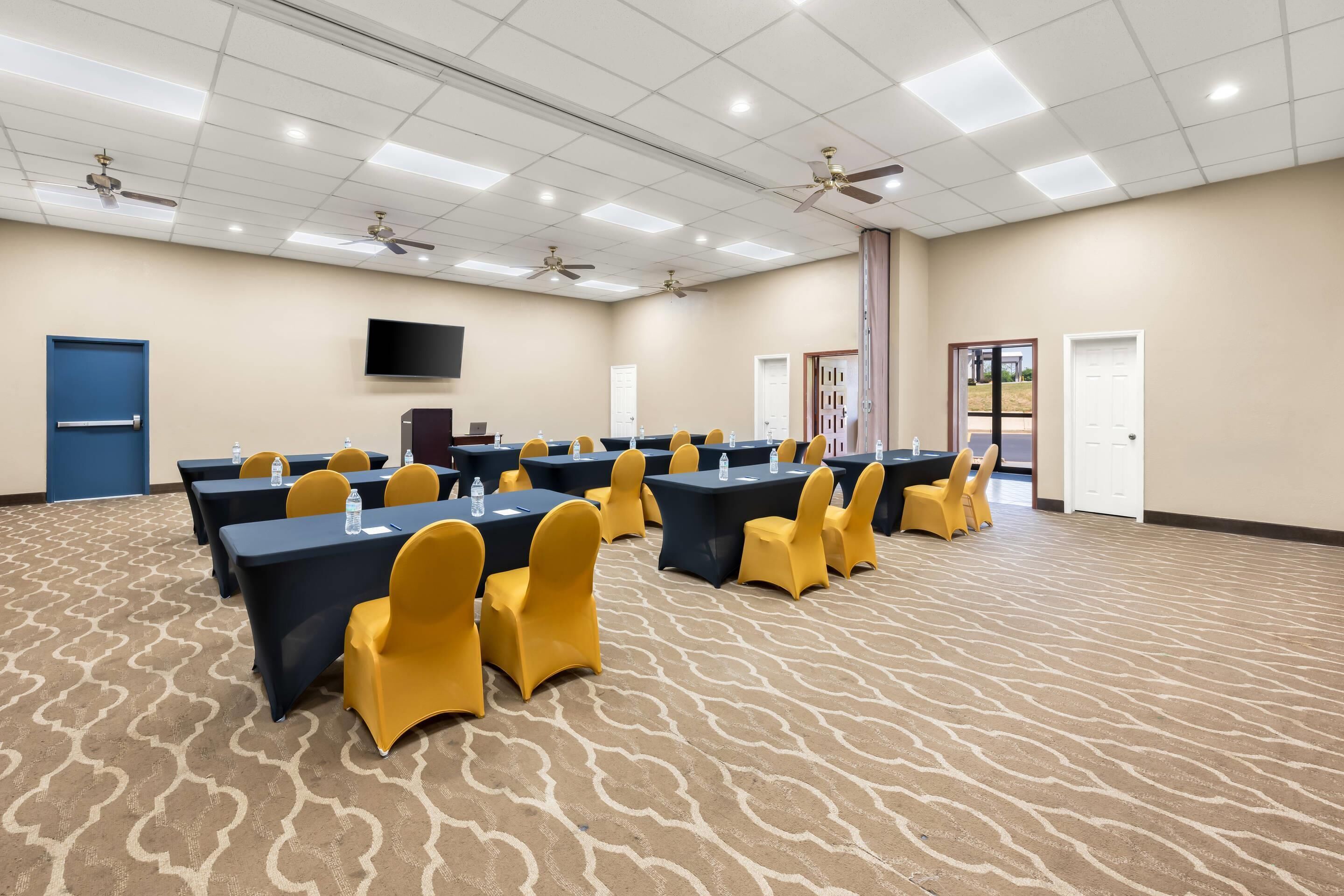 Une salle de conférence équipée de tables, de chaises, de ventilateurs de plafond et d’un téléviseur à écran plat.