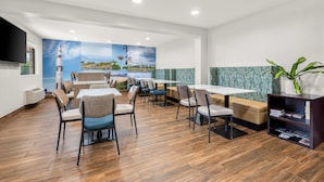 A modern dining area with wooden flooring, multiple tables and chairs, a large mural on the wall, and a bookshelf with magazines. - Clarion Pointe Athens I-65 (Athens)