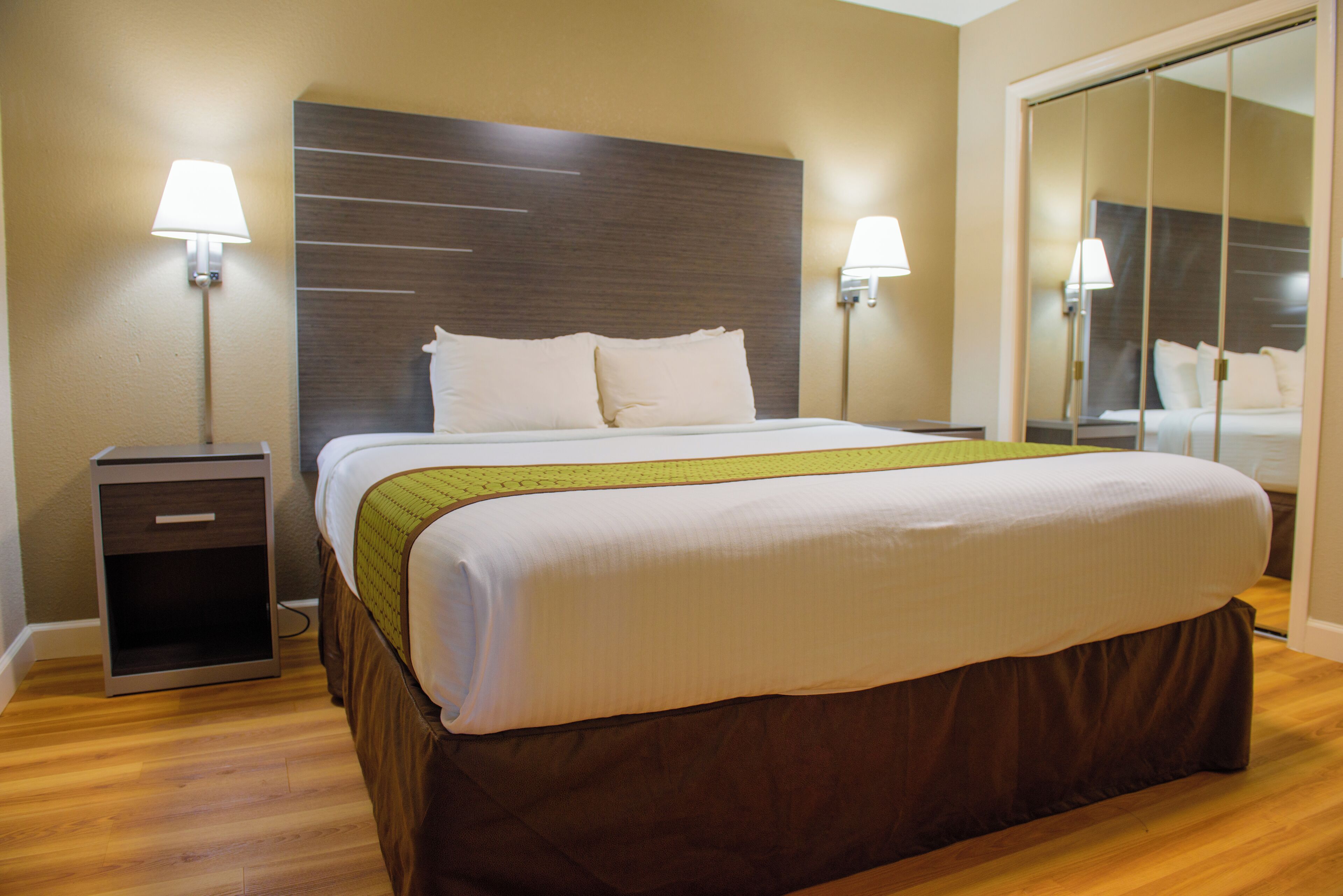 Ein Hotelzimmer mit einem großen Bett, zwei Nachttischlampen, einem Nachttisch und einem Spiegel.