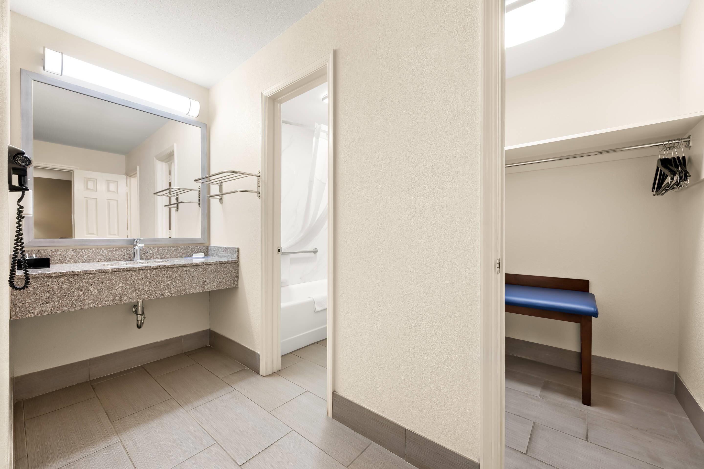 A bathroom with a sink, mirror, towel rack, and a bench.