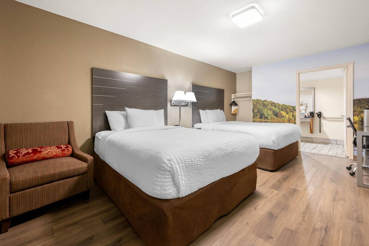 A hotel room with two beds, a sofa, a lamp, and a view of a forest.
