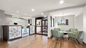 A reception area with a reception desk, a waiting area with patterned chairs, and a view through a glass door. - Clarion Pointe Athens I-65 (Athens)
