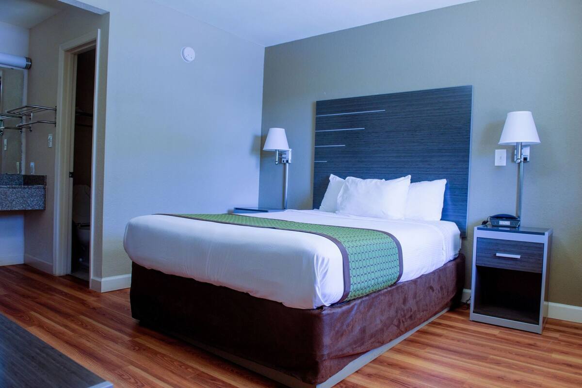 A hotel room with a bed, two bedside tables, a nightstand, a mirror, and a wooden floor.