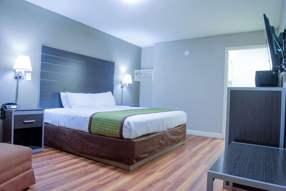 A hotel room with a bed, bedside tables, a desk, a chair, and a TV.