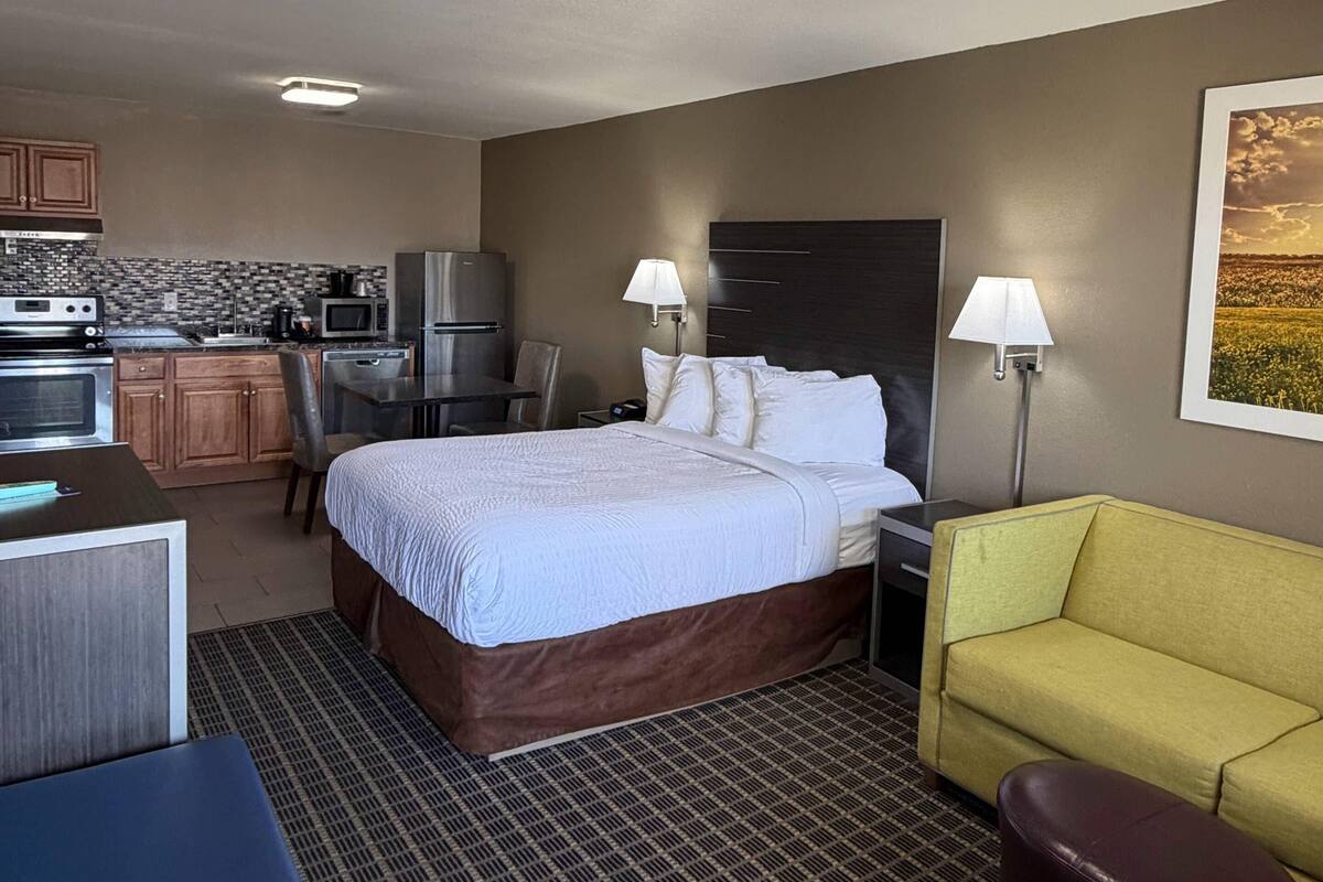 A hotel room with a bed, a desk, a kitchenette, and a sofa.