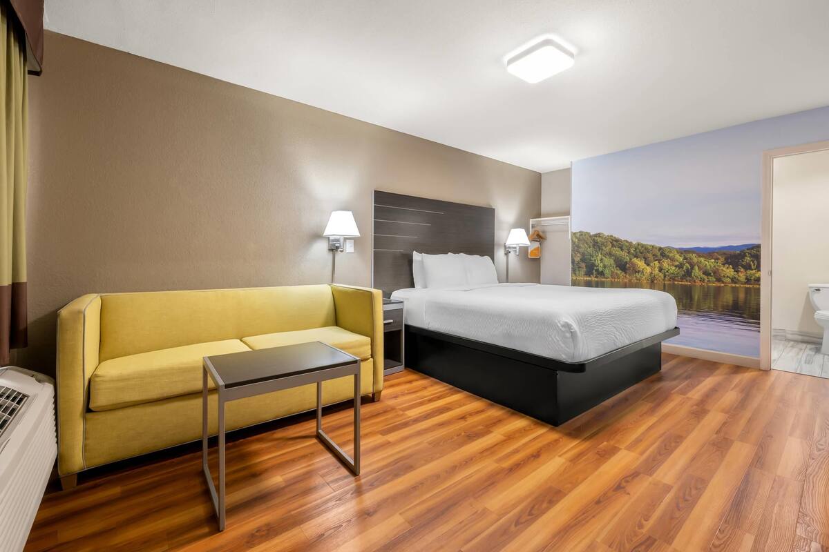 A hotel room with a bed, a sofa, a small table, a nightstand, and a view of a lake.