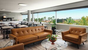A modern hotel lobby with leather sofas, a glass coffee table, and a view of palm trees and mountains.