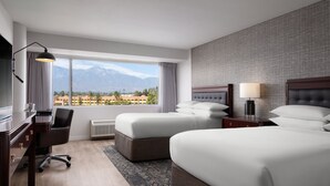 A hotel room with two beds, a desk, a chair, a lamp, and a view of mountains.