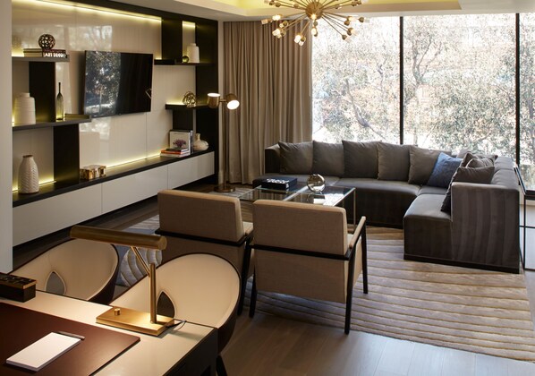 Ein modernes Wohnzimmer mit einer Couch, Sesseln, einem Couchtisch und einem an der Wand montierten Fernseher.