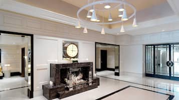 A spacious lobby with a marble fireplace, a large wall clock, and a modern chandelier.