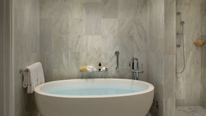 Un baño moderno con una bañera independiente, un estante de vidrio con artículos de aseo y una zona de ducha.