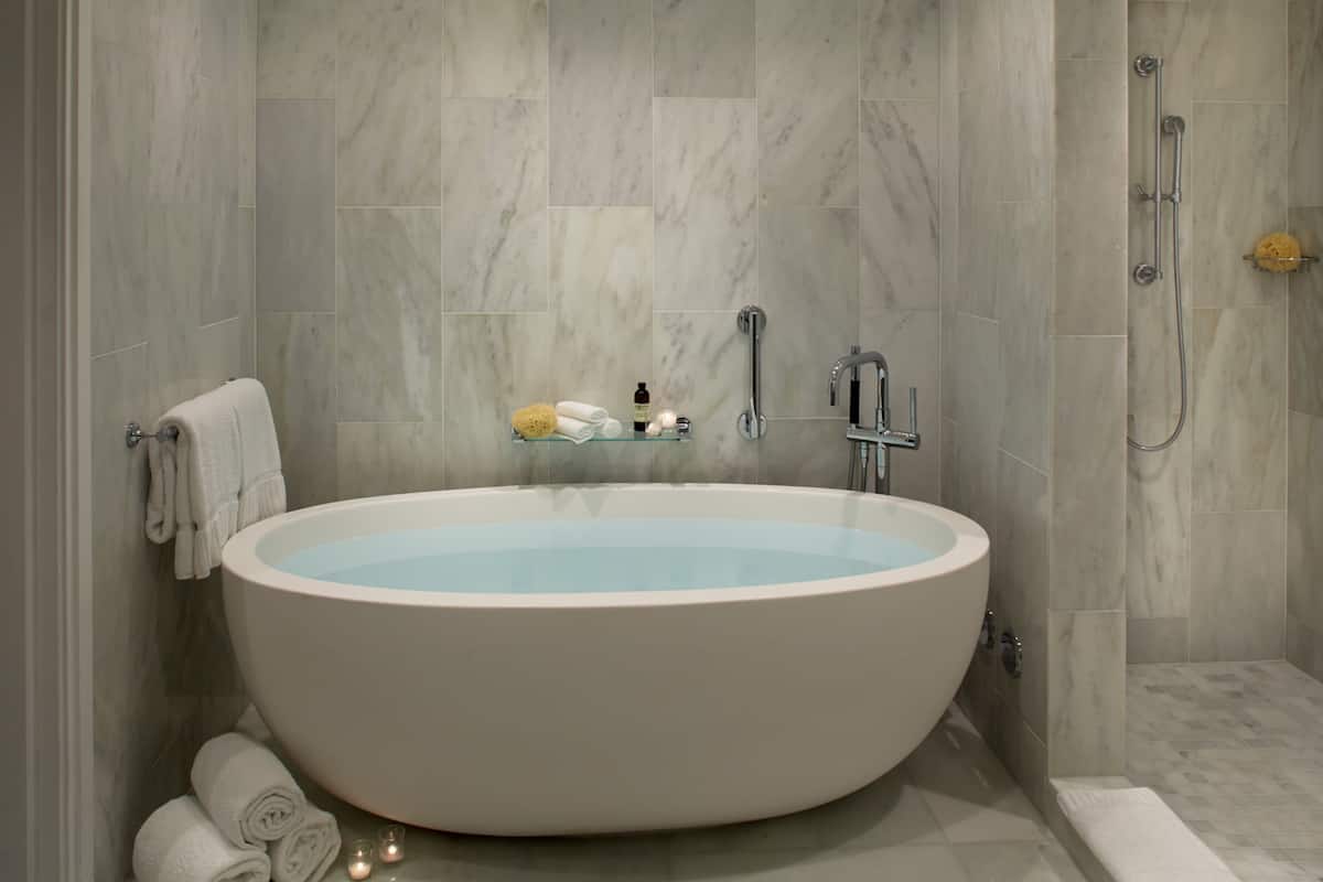 A modern bathroom with a freestanding bathtub, a glass shelf with toiletries, and a shower area.