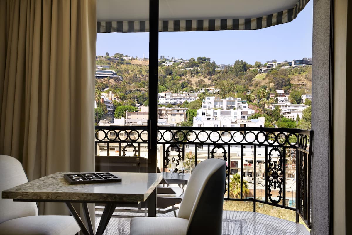A balcony with a table and chairs, offering a view of a residential area with hills and buildings.