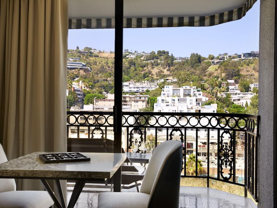 Un balcon doté d’une table et de chaises, offrant une vue sur un quartier résidentiel avec des collines et des bâtiments.