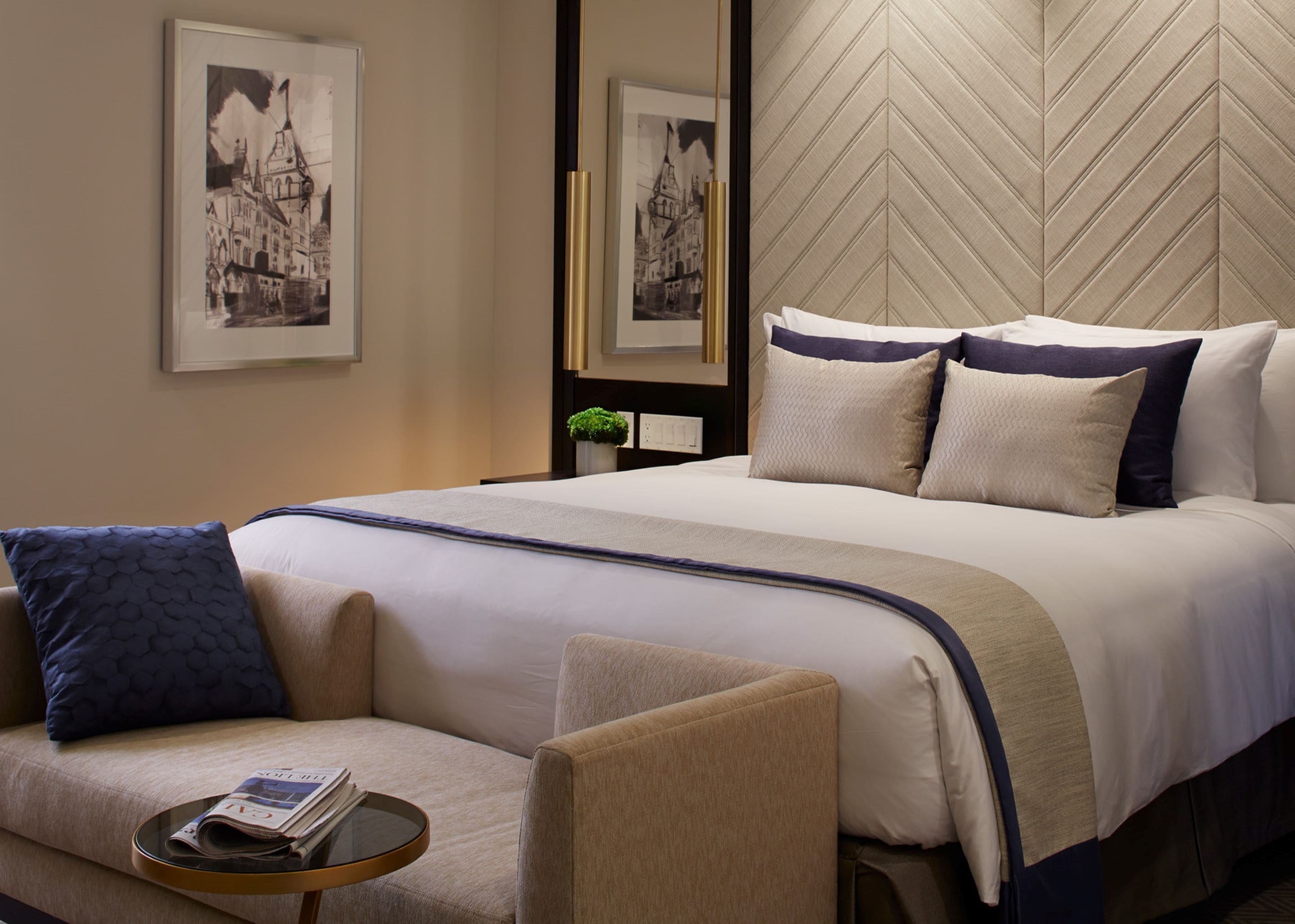 A hotel room with a large bed, a sofa, a small table with a magazine, and a mirror.
