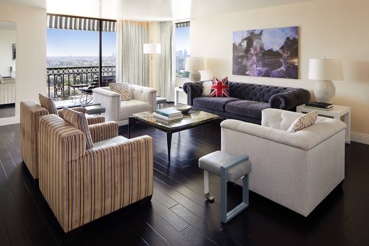 A spacious living room with striped sofas, a grey sofa, and a coffee table. There is a balcony with a view of the city.