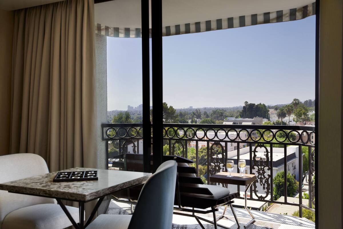 A balcony with a table and chairs, a view of the cityscape, and a curtain partially drawn.