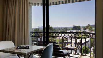 A balcony with a table and chairs, a view of the cityscape, and a curtain partially drawn.