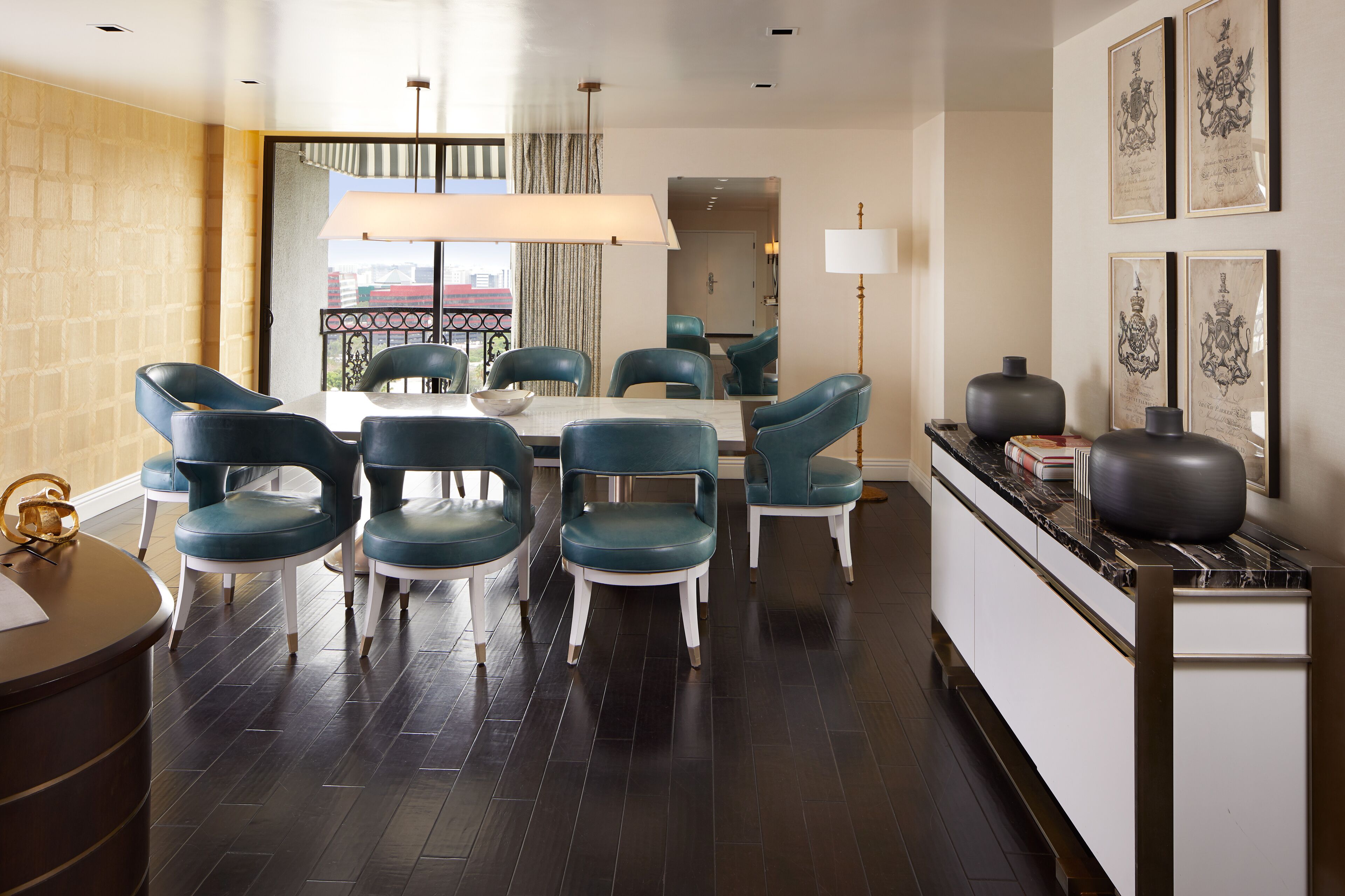 A modern dining area with a round table and six teal chairs, a large window with curtains, and a view of a building outside.