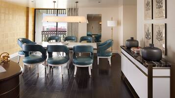A modern dining area with a round table and six teal chairs, a large window with curtains, and a view of a building outside.