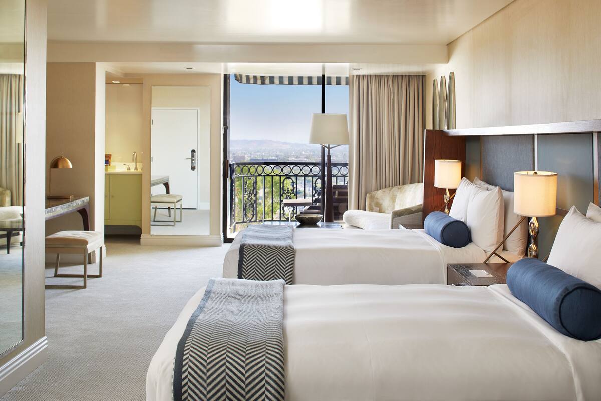 A hotel room with two beds, a balcony with a view, a desk, and a chair.