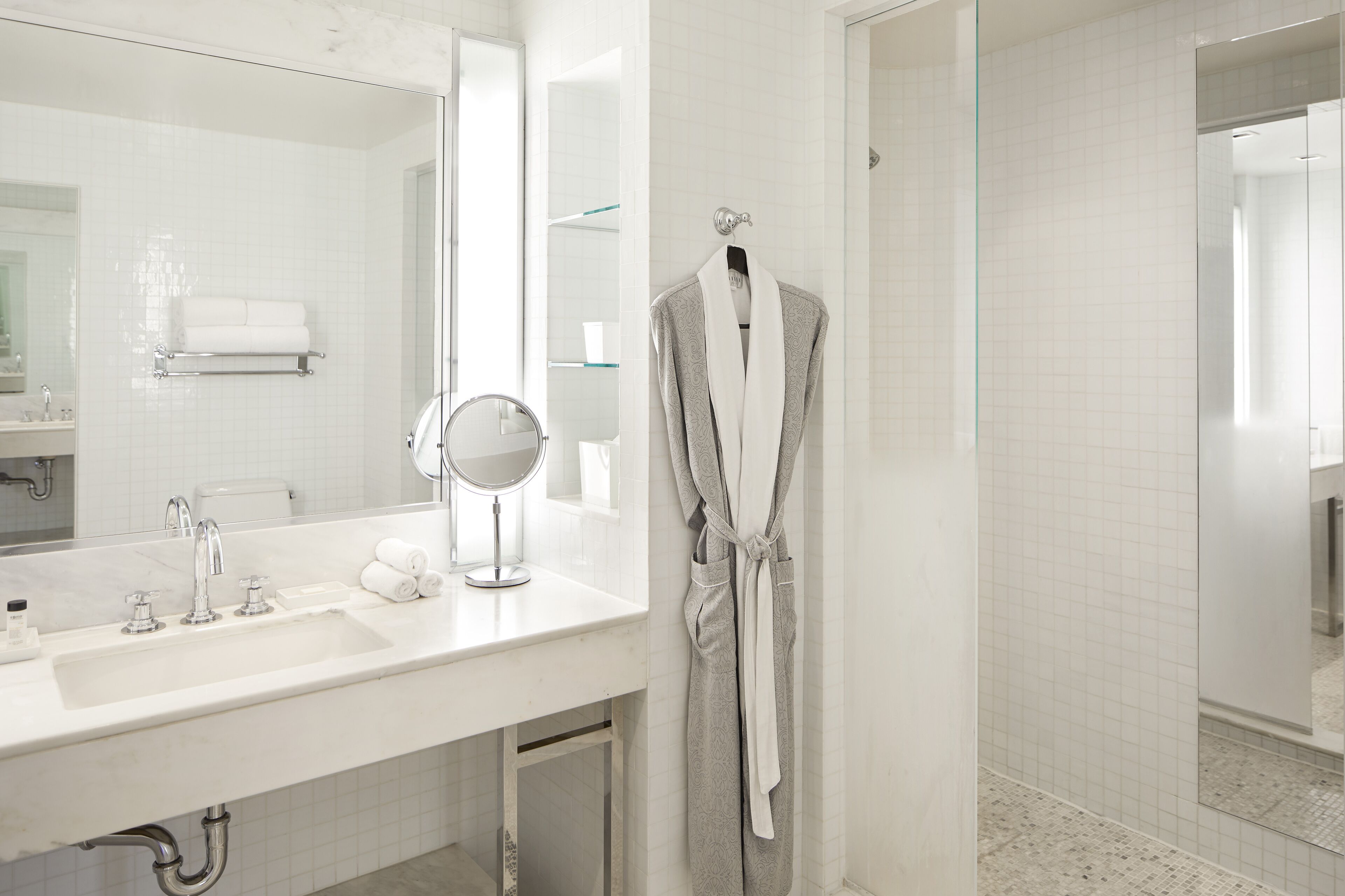 A modern bathroom with a white sink, a mirror, a robe hanging on a rack, and a glass shower enclosure.