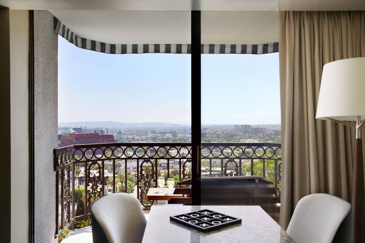A balcony with a table and chairs, a view of the city, and a lamp.