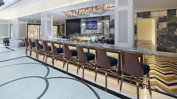 A bar area with a long counter, multiple bar stools, and a television screen.