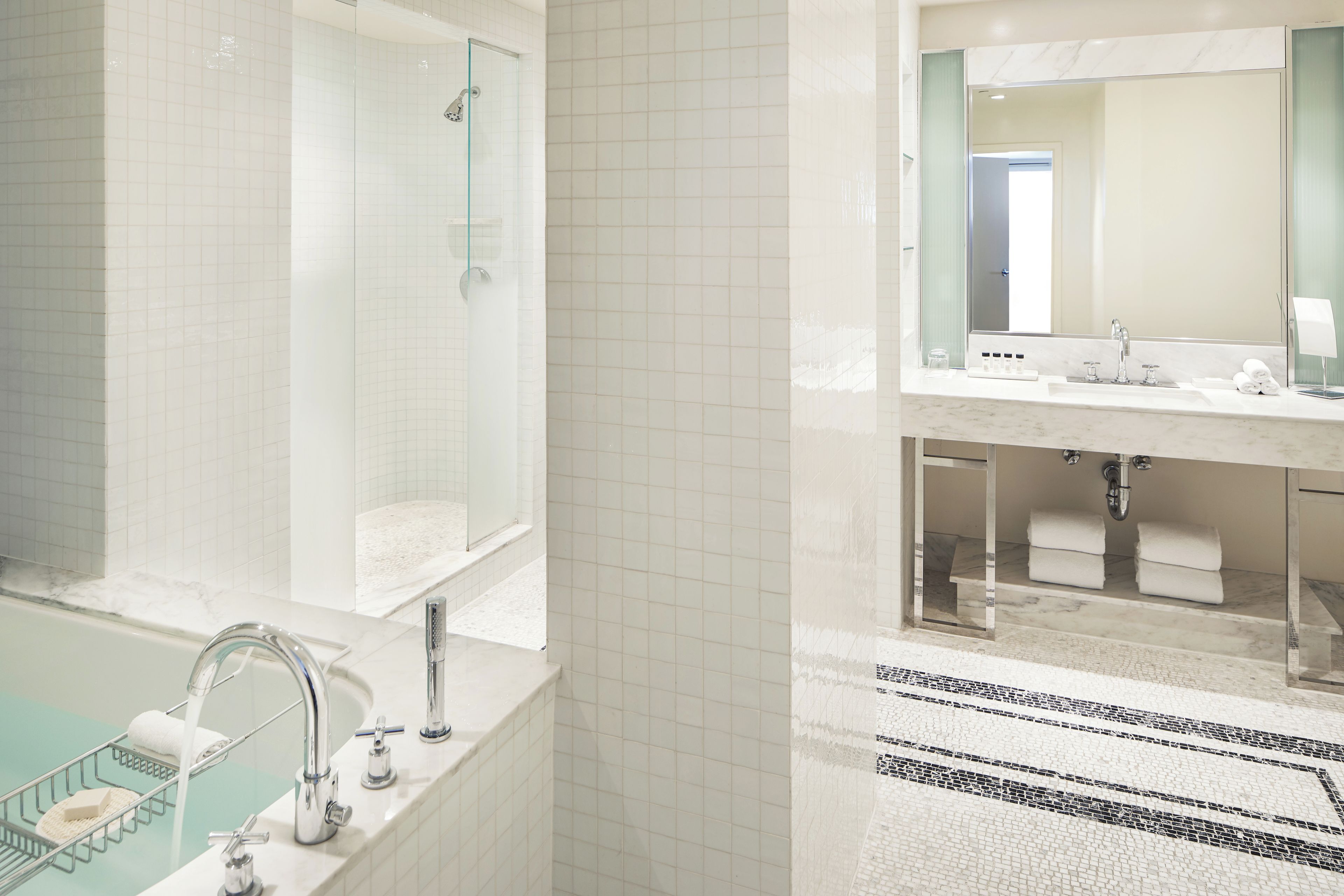 A modern bathroom with a glass-enclosed shower, a marble-tiled floor, and a dual sink vanity with a large mirror.