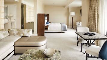 A hotel room with a sofa, a dining table, a bed, a mirror, a lamp, and a view of the outside.