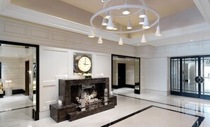 A modern lobby with a marble fireplace, a large wall clock, and a chandelier.