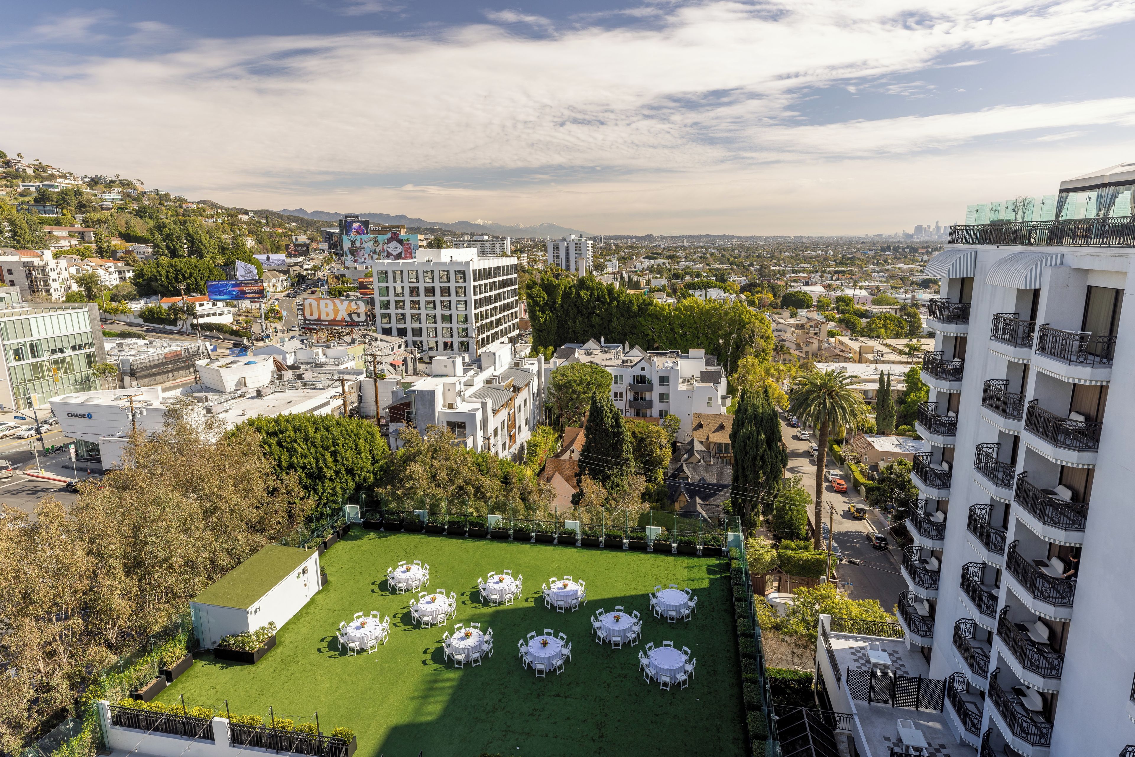 Una terraza en la azotea con varias mesas y sillas redondas, rodeada de edificios y follaje.