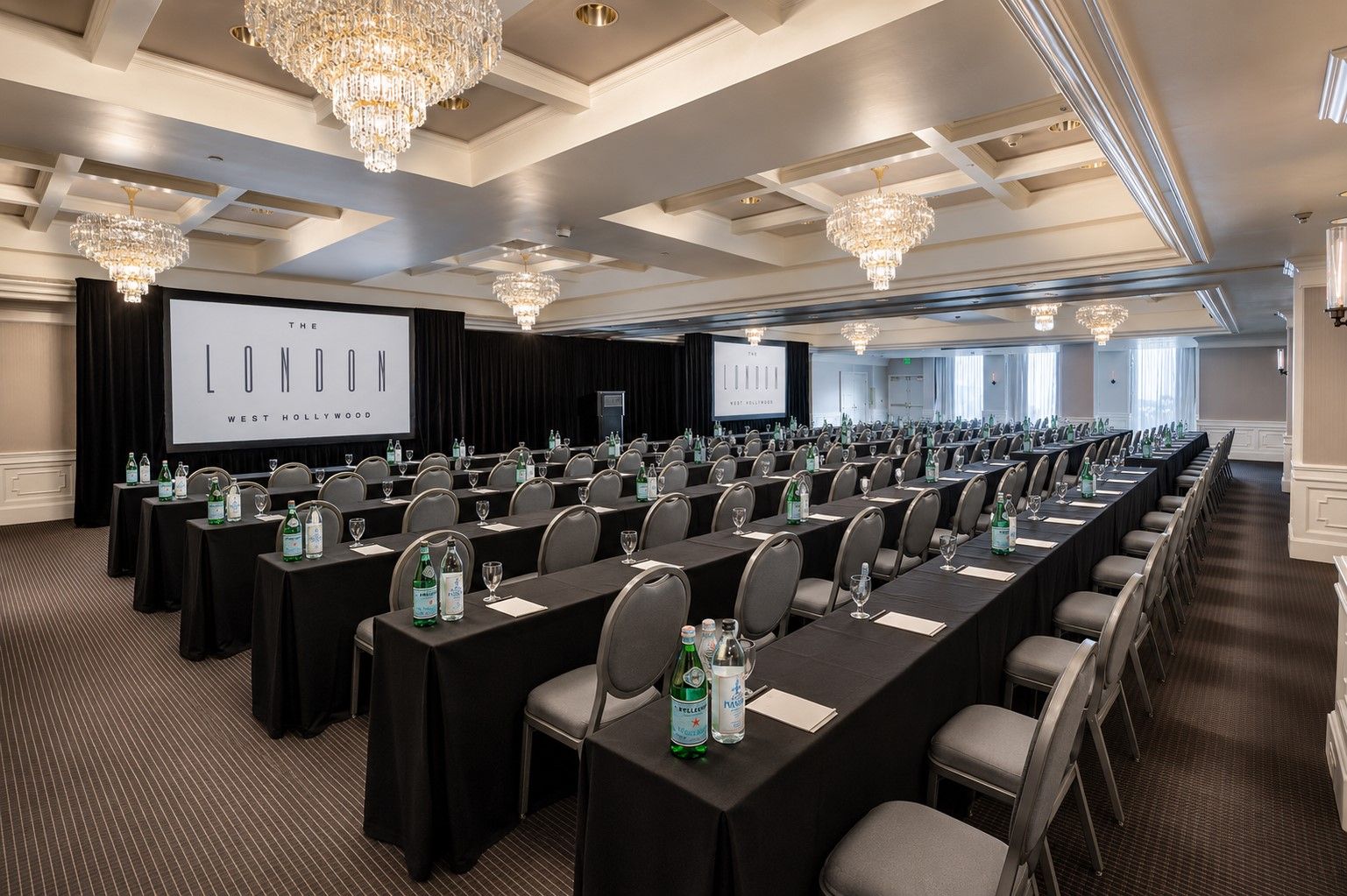 Ein Konferenzraum mit Tischen, Stühlen und einer großen Leinwand, auf der eine Präsentation läuft.