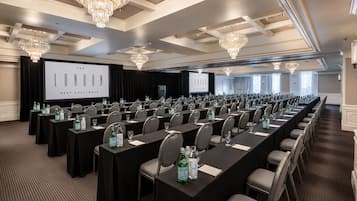 Ein Konferenzraum mit Tischen, Stühlen und einer großen Leinwand, auf der eine Präsentation läuft.