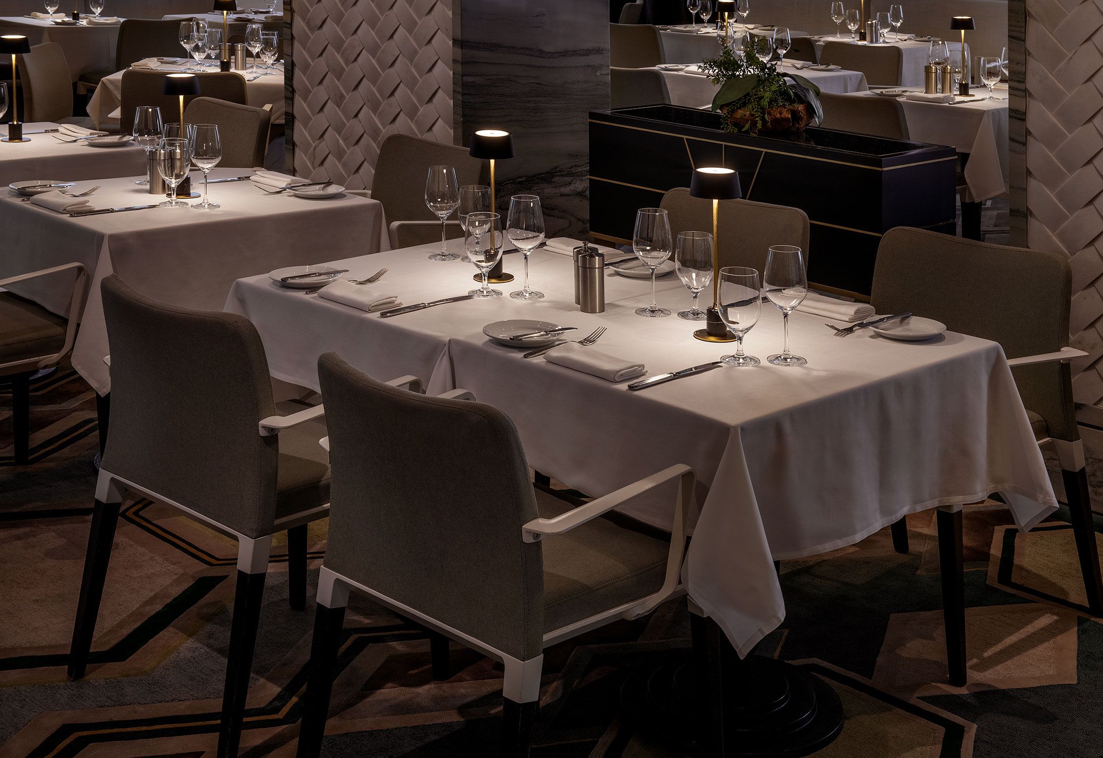 Ein Restaurant mit mehreren gedeckten Tischen, jeweils mit Stühlen, Tischdecken und Geschirr, Bestecke und Gläsern.