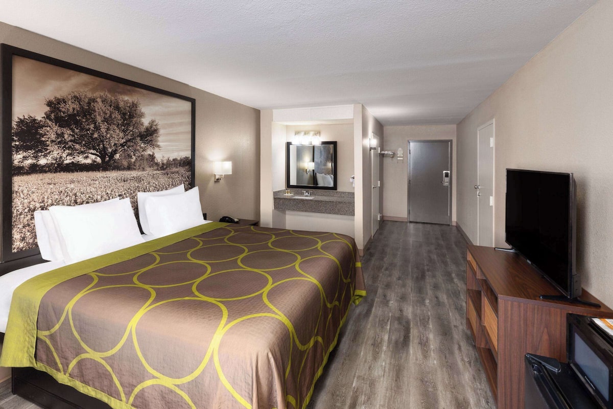 A hotel room with a large bed, a TV, a bathroom with a mirror, and a door leading to another room.