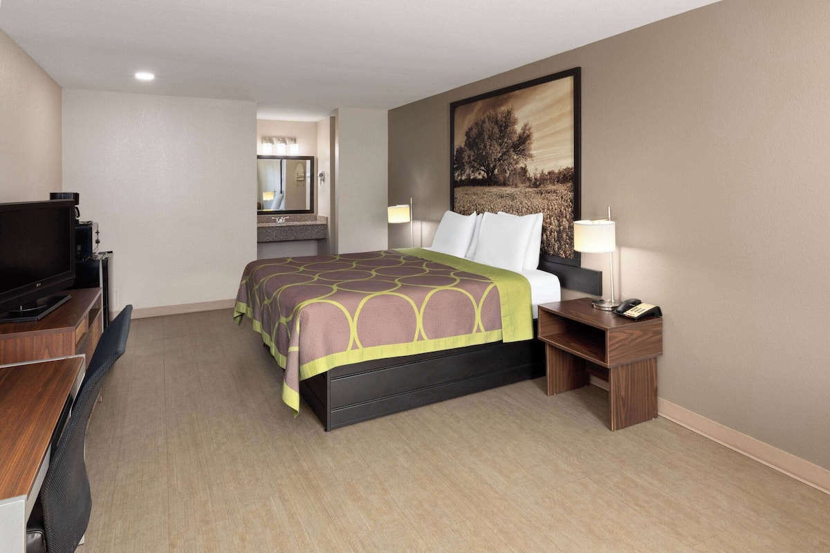 A hotel room with a bed, a desk with a chair, a television, a desk lamp, and a telephone.