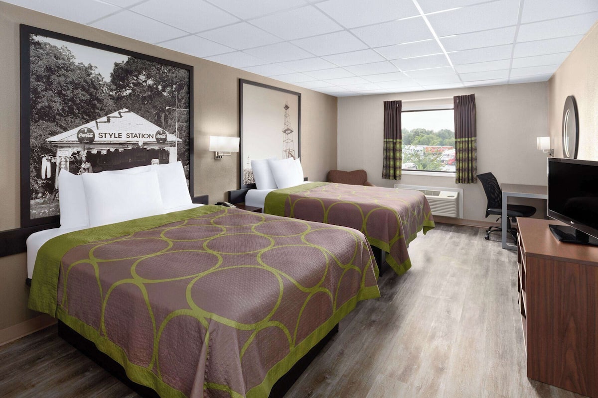 A hotel room with two beds, a desk, a television, and a window with curtains.